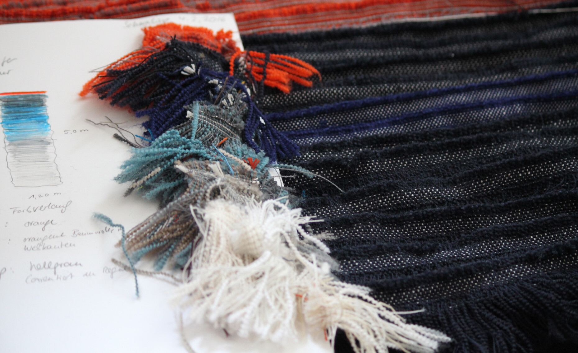 Als Basis für die Teppichherstellung dient eine Zeichnung mit Ölfarben, nach der die schmalen Webkanten per Hand zu einem Farbverlauf kombiniert werden.