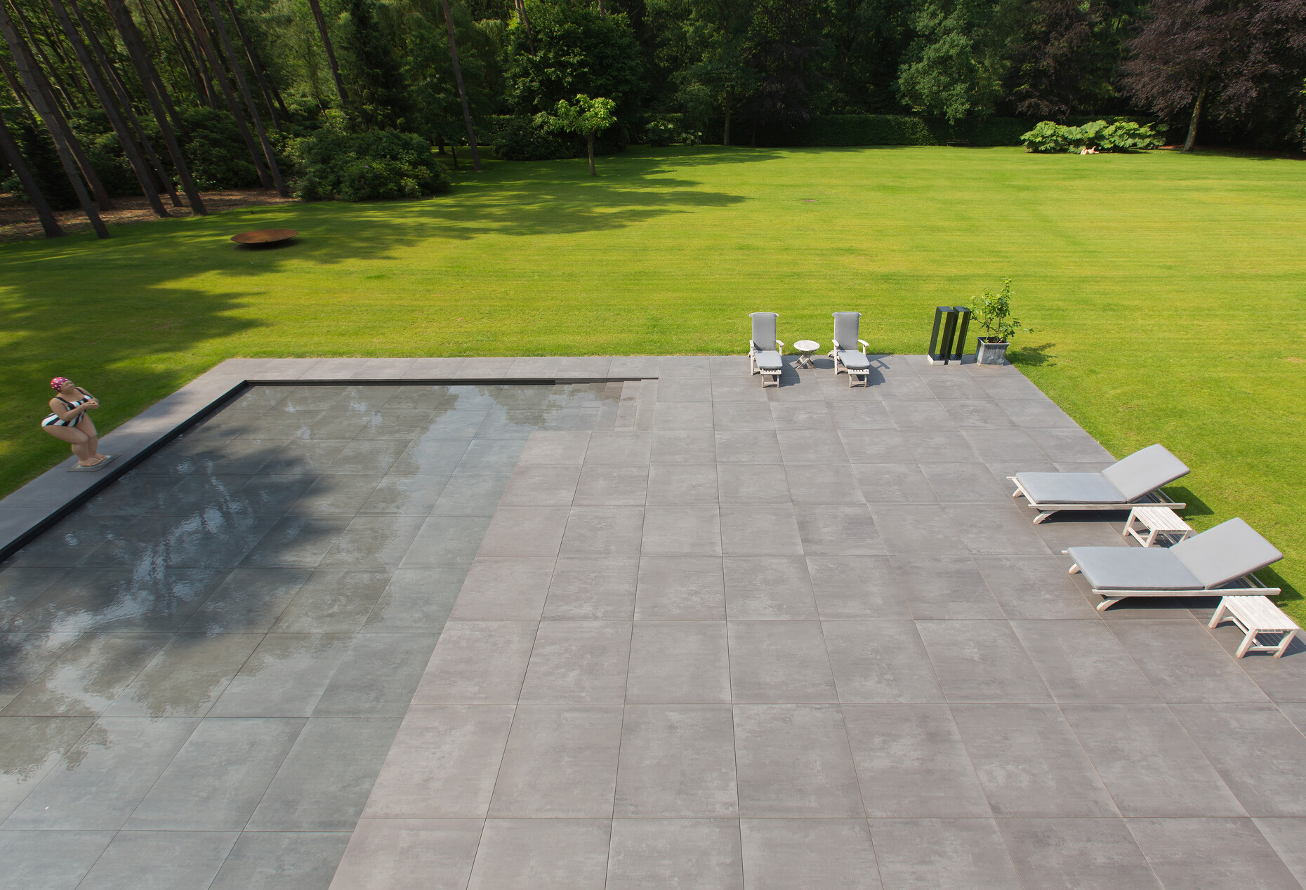 The spacious dark-grey patio with tiles out of the "Ultragres Terra Maastricht"-collection by Mosa, embracing the house like an artificial topographical band and sloping slightly to an expanse of water.