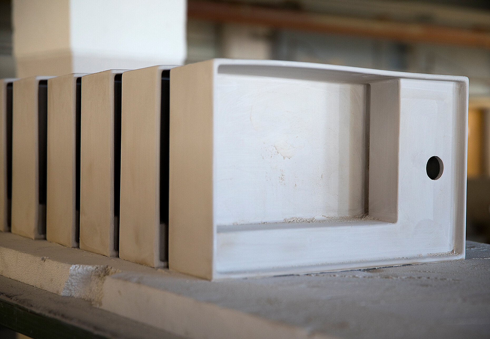 Kartell by Laufen Waschtische aus Saphirkeramik in unglasiertem und unbearbeitetem Zustand. Durch die Vermischung der Tonerde mit dem silikatkeramischem Rohstoff Korund erhält dieses Material nebst seinem porzellanartigen Weiss auch eine besonders hohe Festigkeit, mit der die feine, präzise Formensprache der Waschtische überhaupt erst möglich wird. Der leicht gewölbte Rand an der Waschtischoberkante wird beim Brand durch den Feuchtigkeitsschwund in gerade Form gezogen.