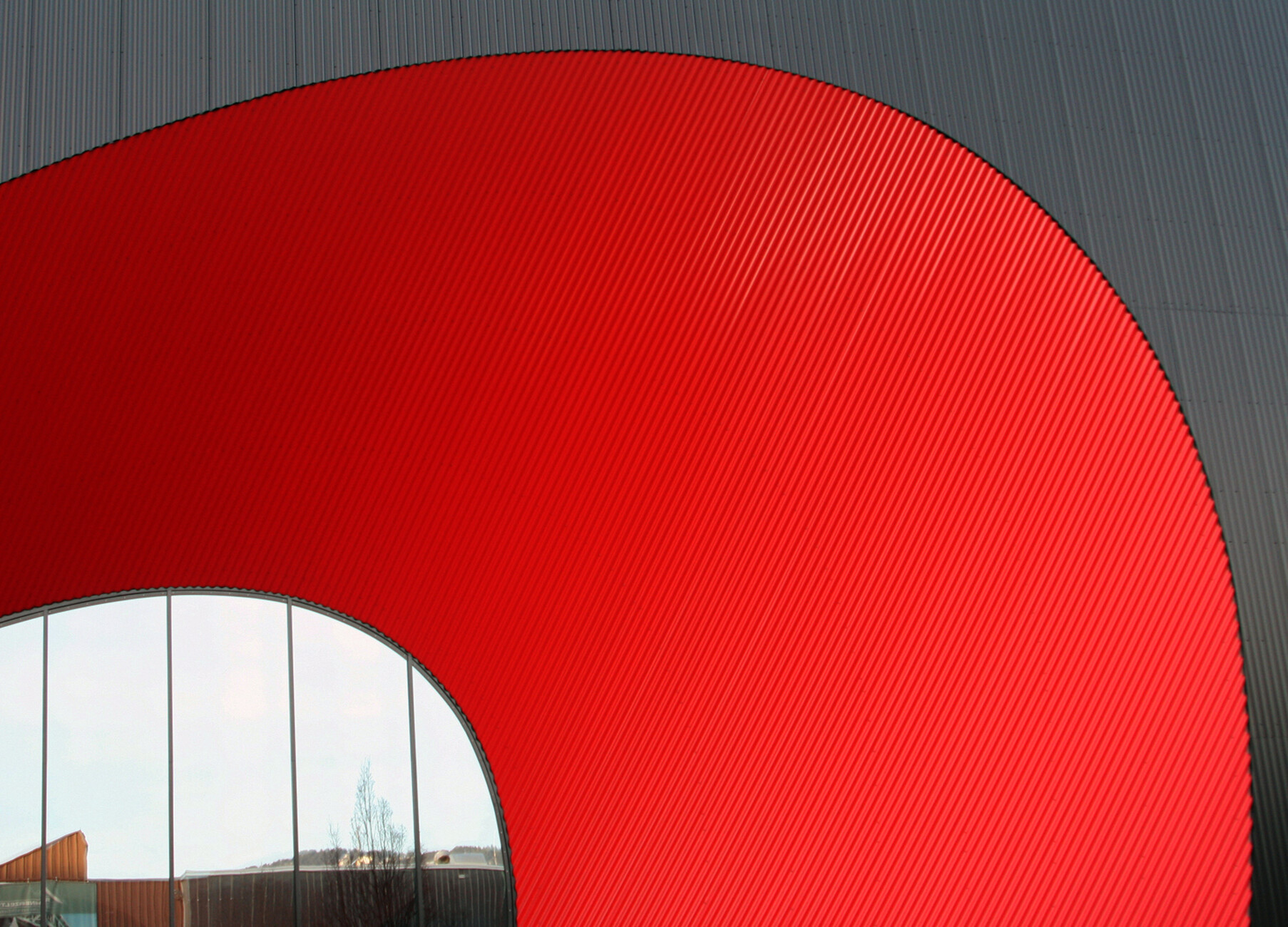 The elliptical entrances to the outdoor area in chimney red create a sweeping contrast to the black-coated outer skin of the rectangular structure.